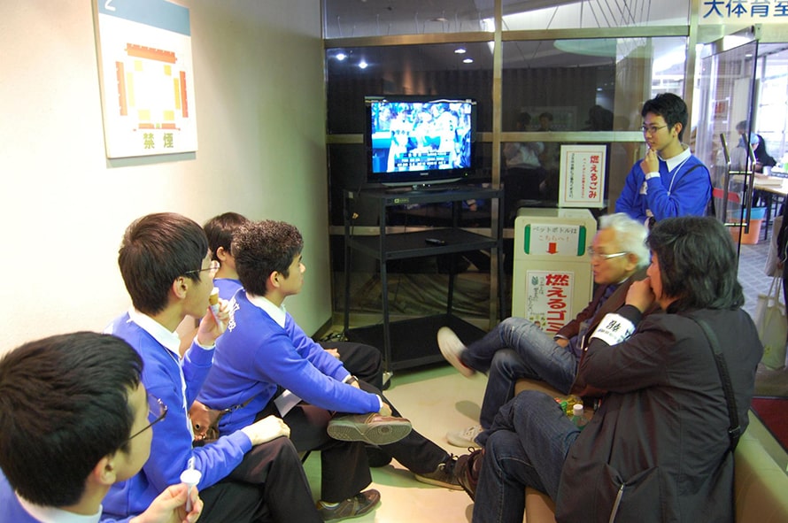 テレビを見る青い服を着た男子生徒と取材記者