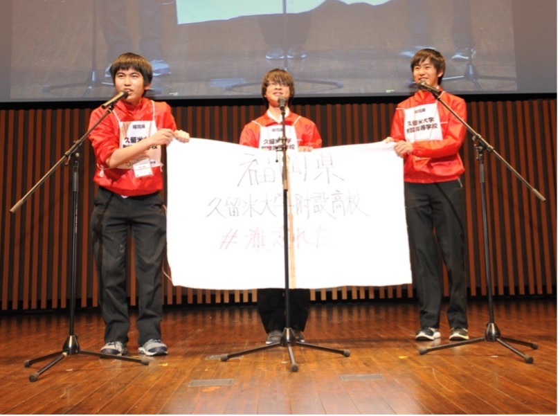 手描きの旗を持ってステージに立つ男子高校生３人